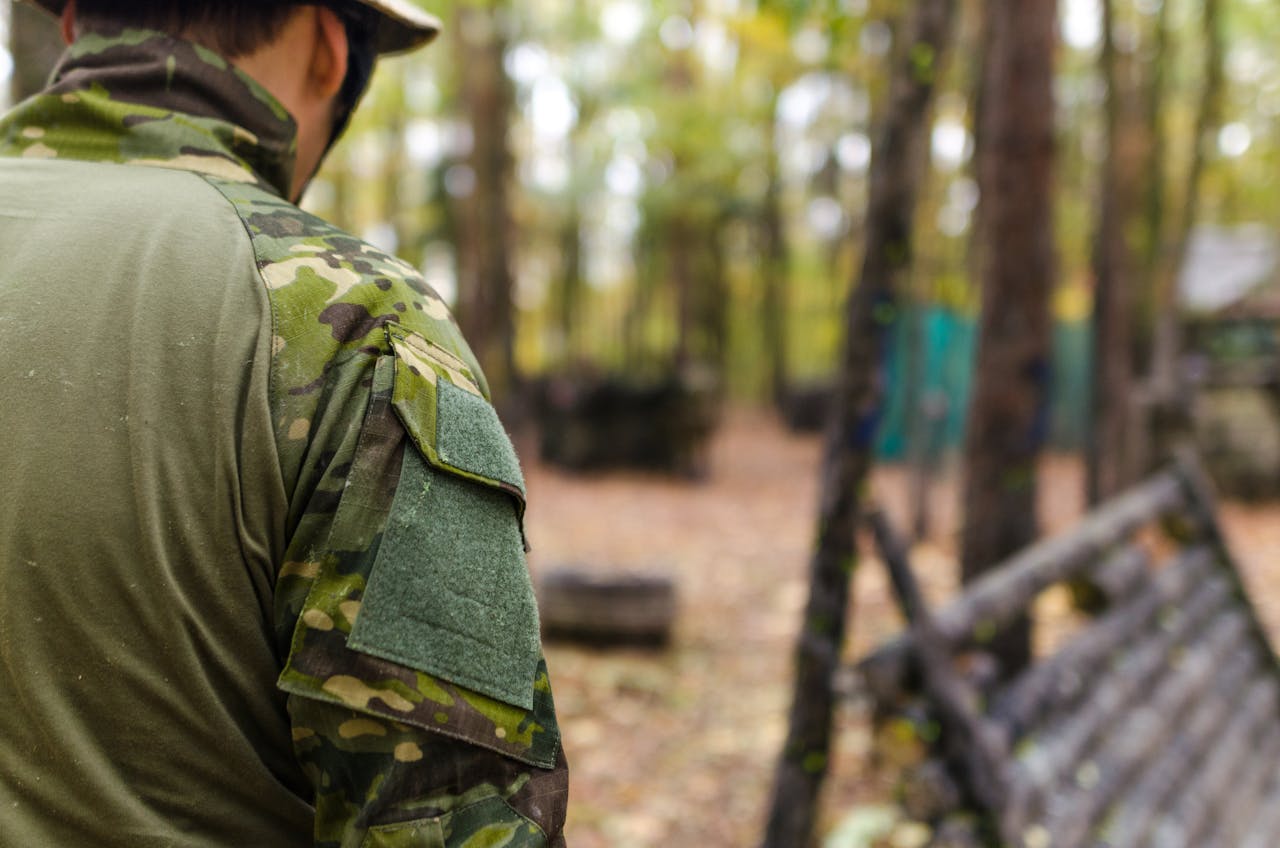 A soldier wearing camouflage preparing for a military exercise in a wooded outdoor environment.